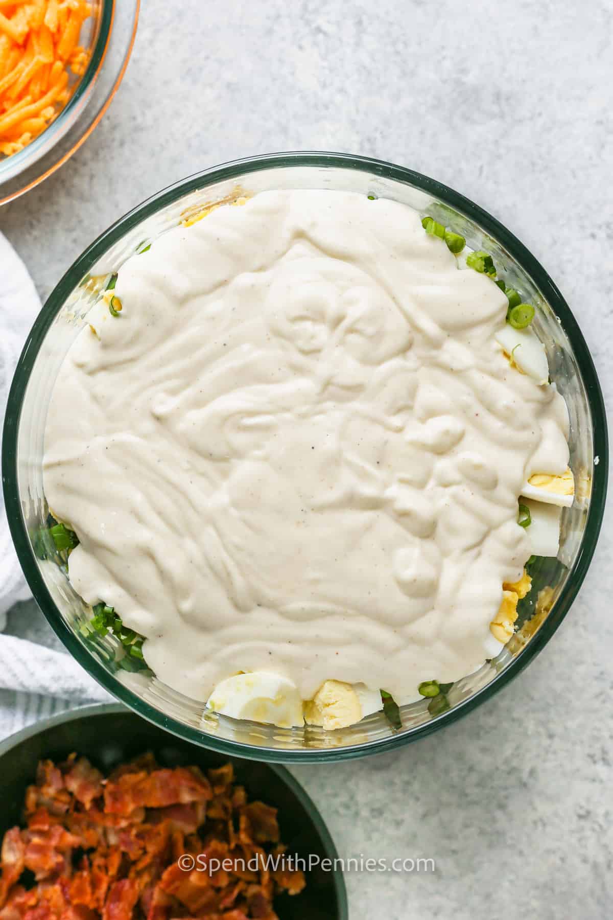 adding dressing over ingredients to make 7 Layer Salad