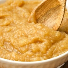 a bowl of homemade applesauce being stirred with a wooden spoon