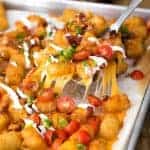 serving up Tater Tot Nachos garnished with green onion and tomatoes, from a baking tray