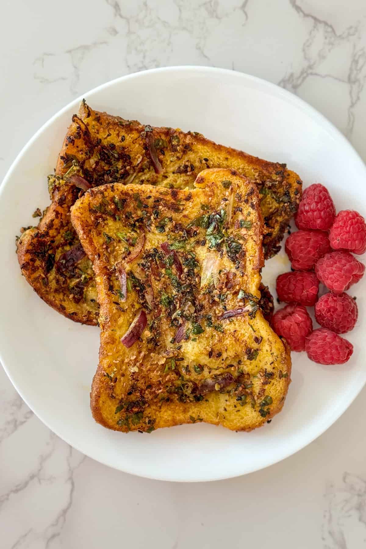 two pieces of savory french toast served with raspberries on the side in a white plate