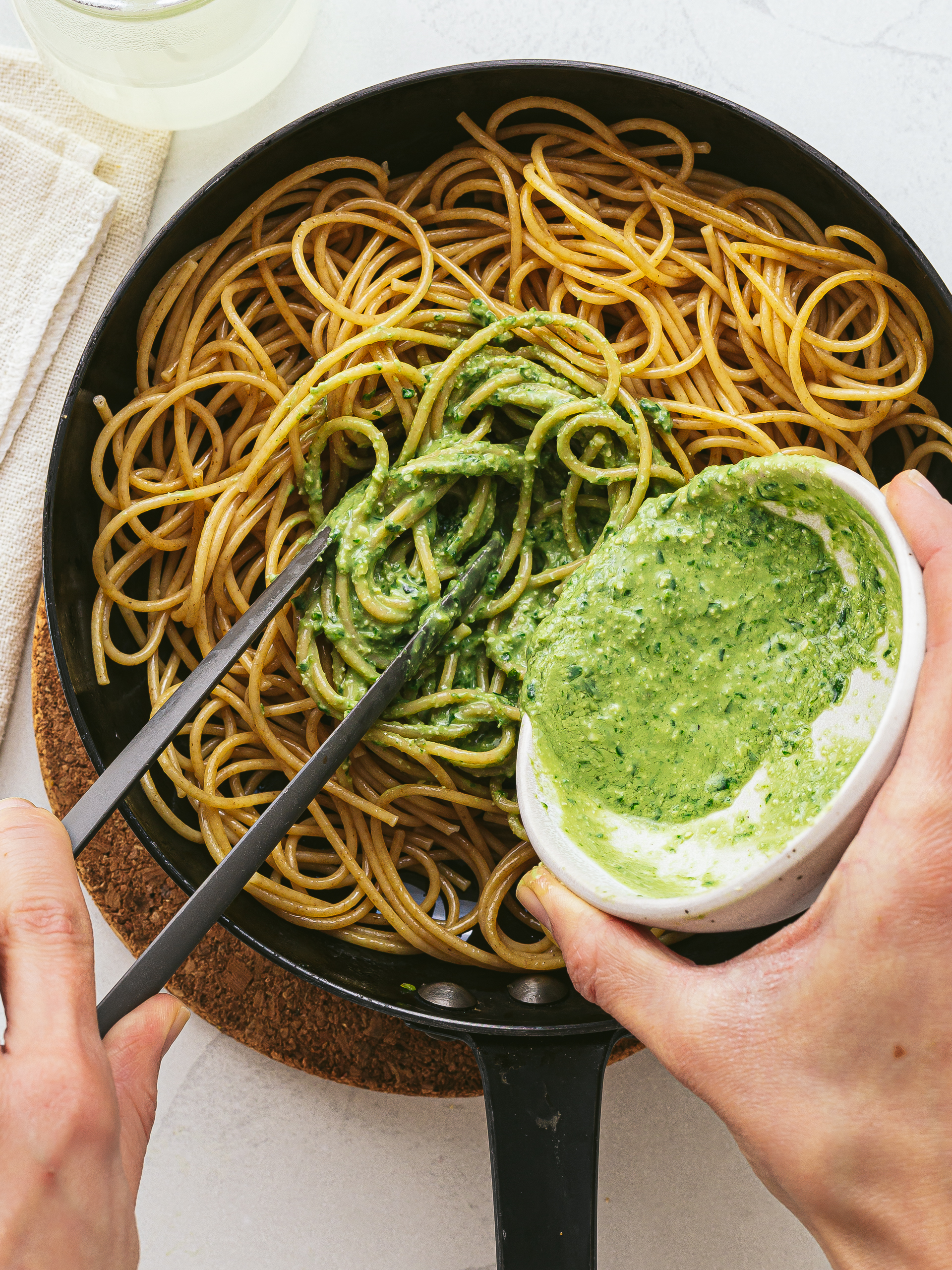 spaghetti pasta mixed with basil pesto sauce in a pan