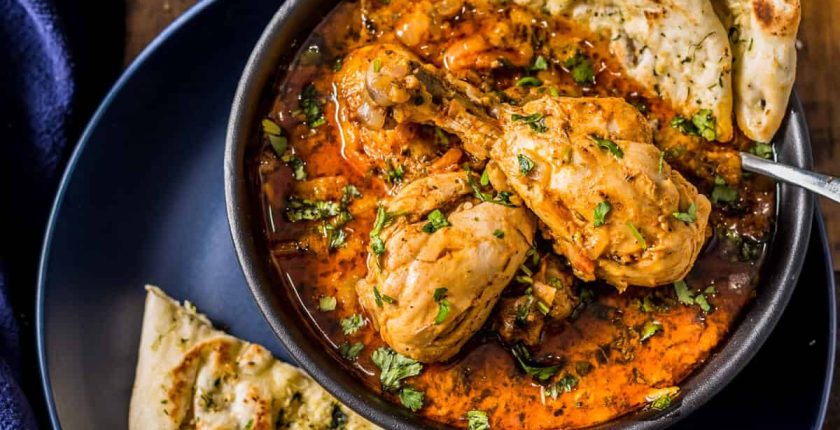 An overhead shot of Indian chicken curry served with naan, rice, lemon wedges and Mango lassi